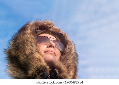 Girl in sun glasses and a fur hood against the blue sky