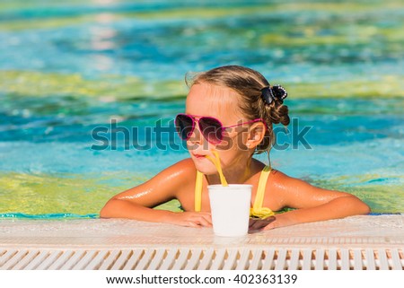 Girl in sunglasses with pigtails drinking juice by the pool on vacation
