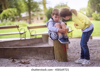 Girl Supporting Sad Boy Sitting Alone On Playground