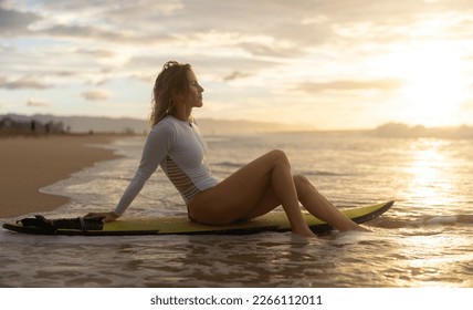 A girl surfer sits on a short surfboard on the beach at sunset. A woman watching the ocean surfing on banzai pipeline north shore Oahu Hawaii. - Powered by Shutterstock
