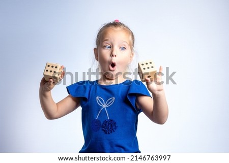 A girl with a surprised look holds playing dice in her hands. The concept of gambling, children's games, probability theory, unexpected luck and winning.