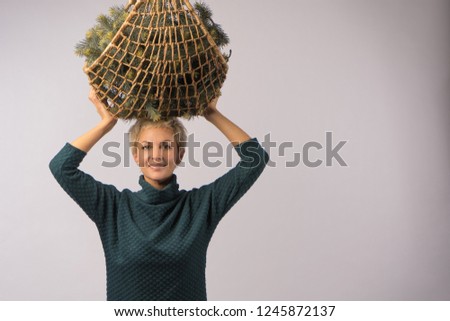A girl in a sweater is holding a basket with pine branches, concept of winter Christmas holidays