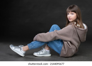 Girl In A Sweatshirt And Jeans On A Gray Background. Beautiful Teen Girl.