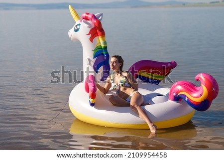 Girl swimming on white, trendy, blown up beach unicorn in summer in a pond, in the sea