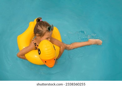 The girl swims swimming in an inflatable circle in the shape of a duck making splashes with her feet. A child sloshing around in a swimming pool
