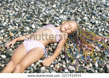 A girl in a swimsuit and Brazilian pigtails lies on a sea pebble