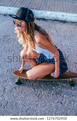 A girl in a swimsuit, riding a skateboard on a longboard, long hair, tanned skin, sunglasses. Against the asphalt road. Concept youth recreation in city. Beautiful european caucasian woman.