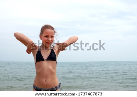 girl in a swimsuit at sea rejoices with hands up
                               