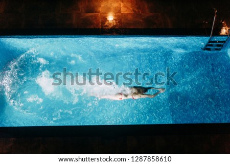 Girl in a swimsuit swimming in the pool at the Villa. Swimming under water in the night.