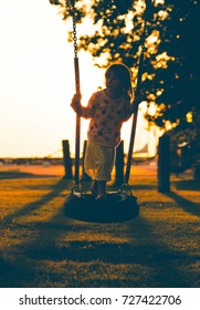 Girl Swinging In Sunset. Kid Playing With Tire Handmade Swing In The Evening. 