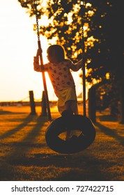 girl swinging in sunset. kid playing with tire handmade swing in the evening. 