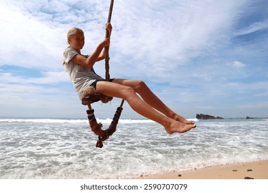 girl swings on a rope by the ocean, enjoying the breeze and the fun. The scene shows a happy summer day, full of adventure and freedom. The beach, waves, and sky create a perfect, relaxing moment