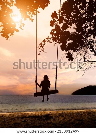 A girl swings on a wooden swing under the tree by the seascape view with the sunset sky on a tropical seashore. Freedom, relaxation, vacation, travel concept.