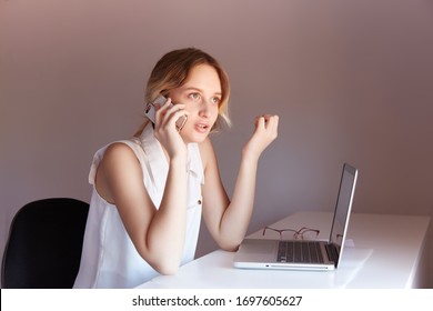 The Girl At The Table During The Day Talks On The Phone. On The Table Laptop And Glasses, Asks A Question, Remote Work Online, Dispute, Finding Out.