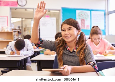 Girl With Tablet Raising Hand In Elementary School Class