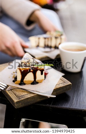 
A girl takes a cheesecake poured with chocolate and mint leaf decoration, next to a cup of coffee