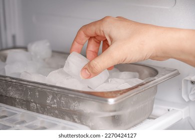 The girl takes frozen ice cubes from the freezer with her hand to prepare soft drinks. - Shutterstock ID 2270424127