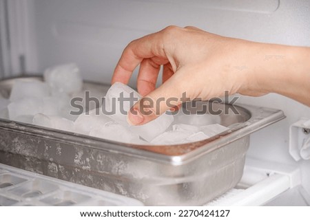 The girl takes frozen ice cubes from the freezer with her hand to prepare soft drinks.