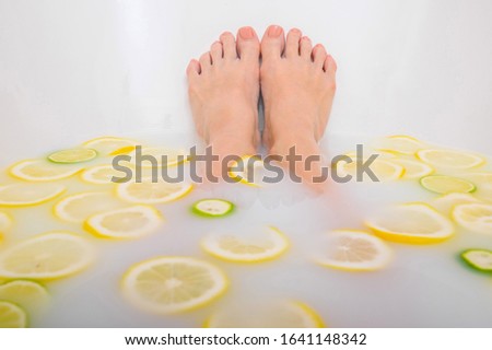 Girl takes a milk bath with lemons and limes. Citrus spa. Body care. Skin whitening. Women's feet.