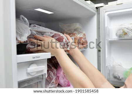 The girl takes out a bag of frozen meat from the freezer in the kitchen at home.