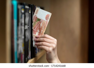 A Girl Takes Out Or Puts Five Thousand Russian Rubles From The Space Between Books On A Shelf. Small Savings