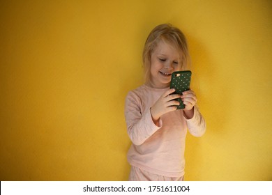  girl takes pictures on a cell phone. Little girl holding a phone in her hands. Girl on a yellow background takes pictures on the phone - Powered by Shutterstock