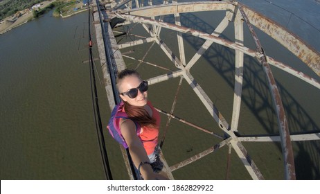 Girl Taking An Extreme Selfie On A Metal Construction, Deep Abyss Underneath Her Feet 