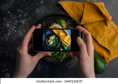 Girl Taking Photo Of Sandwich With Eggs With Smart Phone At Dark Background. Instagram Photography Blogging Workshop Concept.