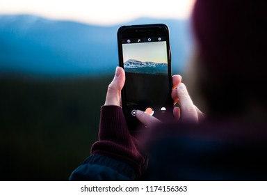 Girl taking photos of the snow-capped mountains using the phone. Close-up shot of the hand holding the phone with the mountain behind.