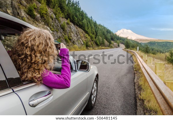 Girl taking pictures of the mount Hood, Oregon from\
inside of the car