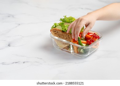 Girl taking, reaching a sandwich, toasts, vegetables, snack. Container, glass box with take away school healthy food. School lunch. Copy space.