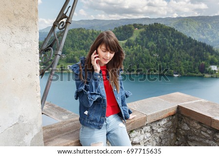 Girl talking on the phone from castle top of the mountain with valley view and lake on the background. copy space