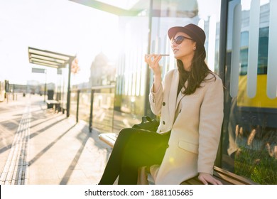 Girl talking on the phone on the speaker while sitting at the bus stop - Powered by Shutterstock