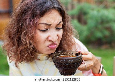 The Girl Tastes Bitter And Strong Pu-erh Tea Or Coffee And Makes A Disgruntled Face.