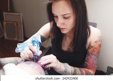 Girl tattoo artist works on a tattoo on a man's hand