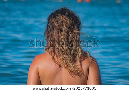 Girl with a tattoo on a beach in Croatia, sitting with her back. Beautiful color of water. Holiday at the seaside.