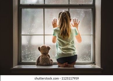 Girl and teddy bear looking out window