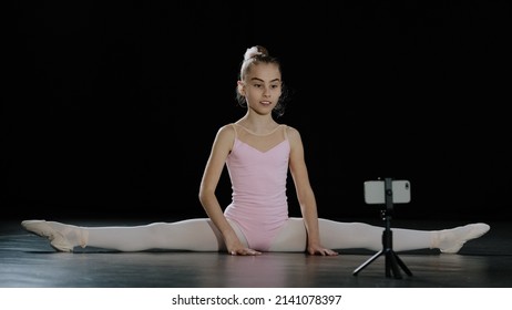 Girl Teenager Child Ballerina Acrobat Gymnast Sits On Floor Dance Class Online Lesson With Internet Coach Trainer Teacher Remotely With Smartphone On Tripod Sitting On Twine Recording Video Vlog Blog