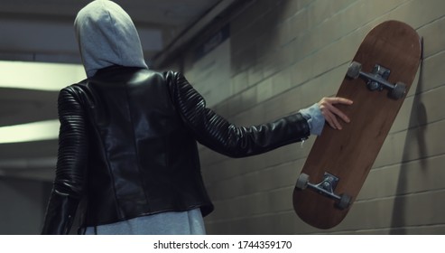 Girl teenager goes at night in the underpass. Young caucasian woman with skateboard in dark underground tunnel. Urban city lifestyle. Back view - Powered by Shutterstock