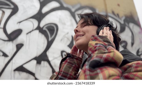 girl teenager in headphones on the background of graffiti smiles. music art freedom youth concept. brunette teenager girl walking past a wall with graffiti listening music with headphones lifestyle - Powered by Shutterstock
