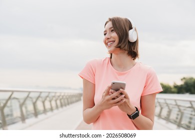 Girl teenager woman student walking in the city listening to the music in headphones earphones using smart phone for musical application, searching for favorite soundtrack singer song outdoors. - Powered by Shutterstock