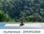The girl testifies sitting on the rug in the lotus position on the background of the tropical jungle. Back view
