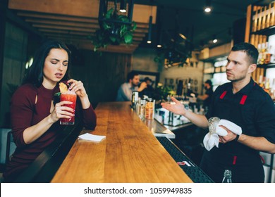 A Girl That Is Not Satisfied With The Cocktail That Barman Has Made For Her. She Looks Dissapointed. But Barman Looks Sad As Well Because He Doesn't Agree With His Customer.