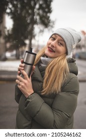 A Girl With A Thermos In Her Hands Walks Around The City And Enjoys The Winter Weather. Great Winter Mood. The Girl Is Enjoying The Snow And Drinking Hot Coffee. Winter Fashion.