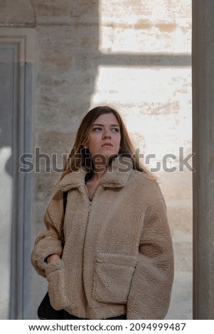 A girl with a thick winter coat. She looks pretty worried. She is afraid that someone will come. She looks far away.