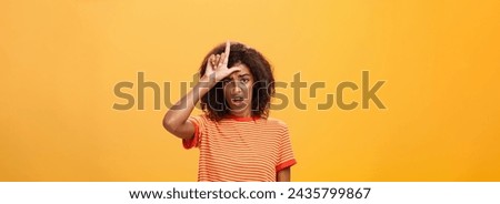 Girl thinks she loser. Portrait of gloomy bothered and displeased african american woman with afro hairstyle showing l word over forehead complaining feeling gloomy and unhappy over orange background.