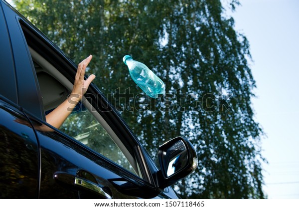 A girl\
throws an empty plastic bottle into the open window of a car. A\
flying object is slightly blurred. Bottom view, against the\
background of blurry trees and sky, summer\
day