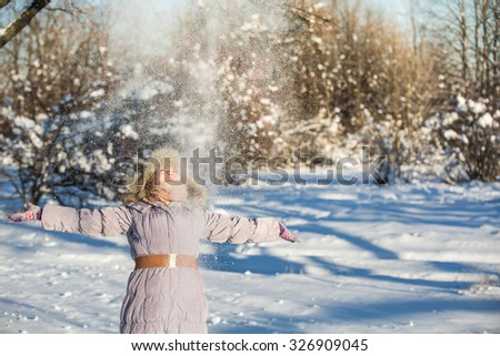 Girl throws snow up. Photographed in direct sunlight. Silhouette. Girl in the park, around the snow. One can see a grain of snow fluttering around.