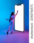 Girl touching giant 3d model phone screen against blue studio background in neon light. Online services and apps. Concept of human emotions, business, sales, shopping, Internet, lifestyle, youth, ad