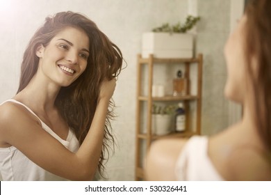 Girl touching her hair and smiling while looking in the mirror 